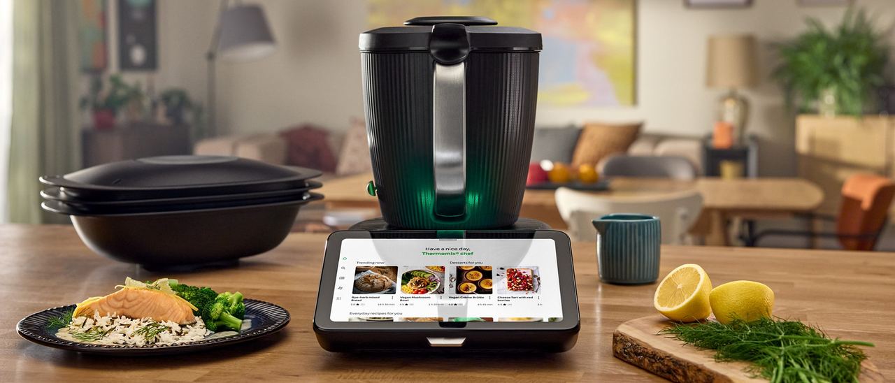 Thermomix TM7 oficial sobre una encimera de cocina con salmón, verduras y accesorios